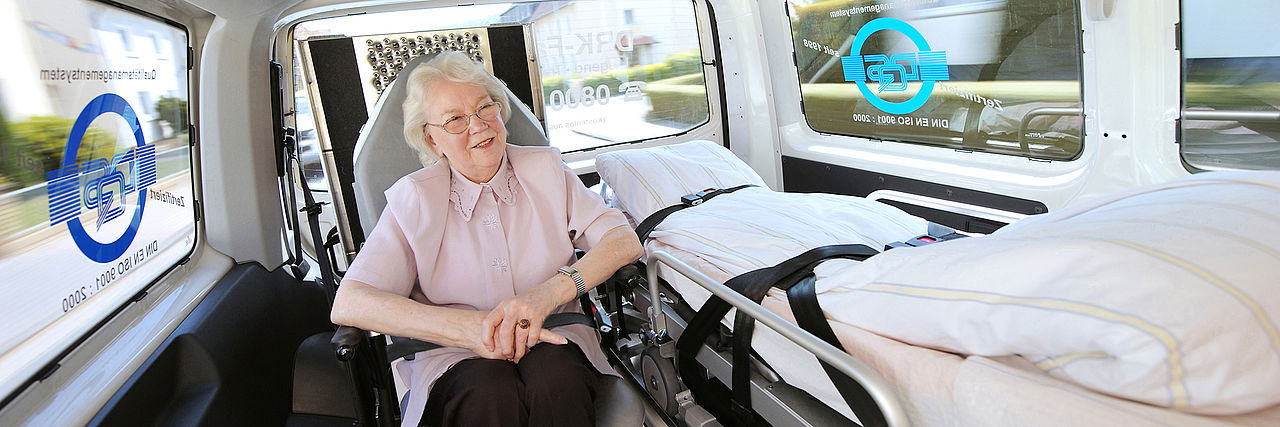 Portrait einer lächelnden Seniorin in einem Fahrzeug des DRK Krankentransportes.